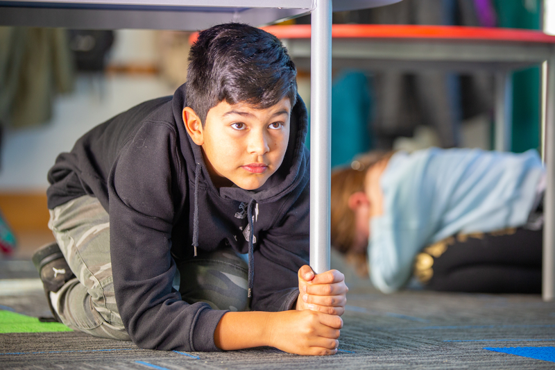 Two children doing Drop, Cover and Hold under a table