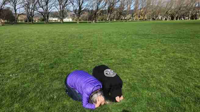Two people doing Drop, Cover and Hold in an empty park